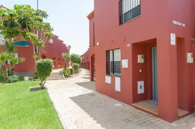 a red building with a sidewalk next to a yard at Adosado Dulce Barrosa in Chiclana de la Frontera