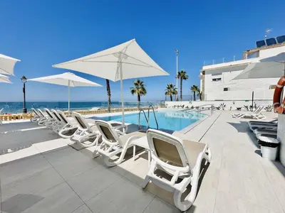 a row of white chairs and a swimming pool at Hotel Apartamentos Marina Luz in Chipiona