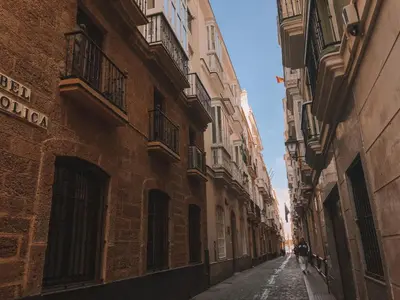 an alley with buildings and a person walking down the street at Apodaca Rooms in Cádiz