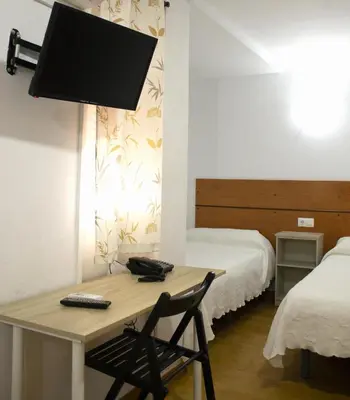 a room with a desk with a television and a bed at Hostal Villa in Chiclana de la Frontera