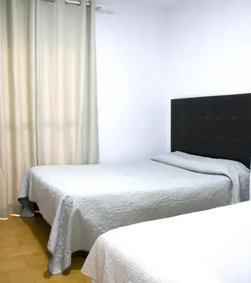 two beds in a room with white walls and curtains at Hostal Villa in Chiclana de la Frontera