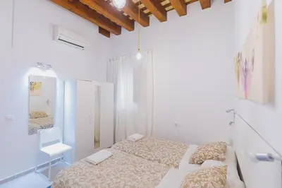 a white bedroom with a bed and a chair at Apartamentos casa palacio in El Puerto de Santa María