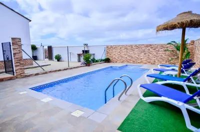 a swimming pool with chairs and an umbrella at Casa Manoli in Conil de la Frontera