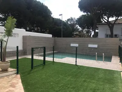 a tennis court behind a fence with grass at Villa Chill In in Chiclana de la Frontera