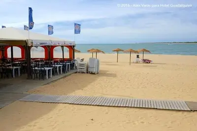 a beach with tables and chairs and umbrellas on the beach at Playa de Las Piletas in Sanlúcar de Barrameda