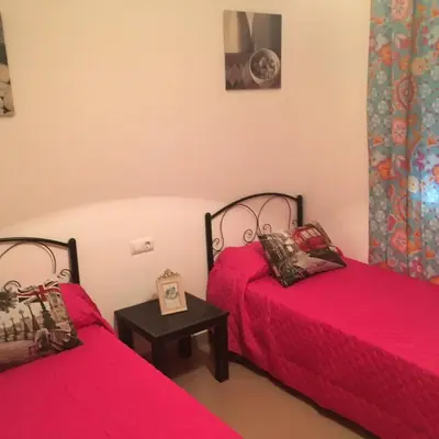 a room with two beds with red sheets and a table at Playa de Las Piletas in Sanlúcar de Barrameda
