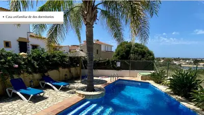 a swimming pool with two chairs and a palm tree at Arco Casas Adosadas in Conil de la Frontera