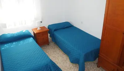 two beds in a bedroom with blue sheets and a night stand at APARTAMENTO VILLA DE ROTA - VISTA MAR, 135m2, Terraza, SAT TV y más in Rota
