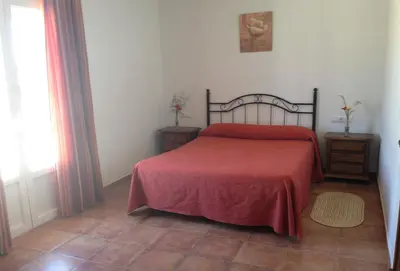 a bedroom with a bed with a red blanket and a window at Casa Rural El Limonero in Los Naveros