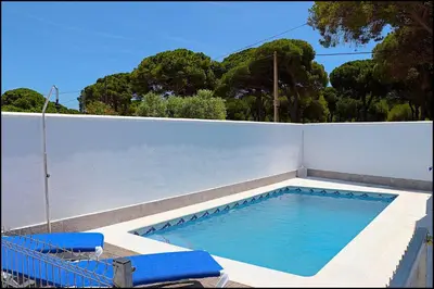 a swimming pool with two blue chairs next to a wall at Casa Rural Zara I in Conil de la Frontera
