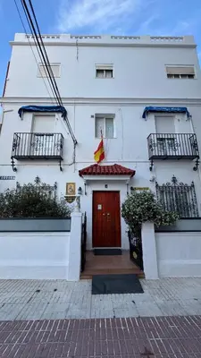 a white building with a red door and two balconies at Hostal Playa Hidalgo in Rota