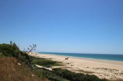 a beach with people sitting on the sand and the ocean at Casa Jorge in Conil de la Frontera