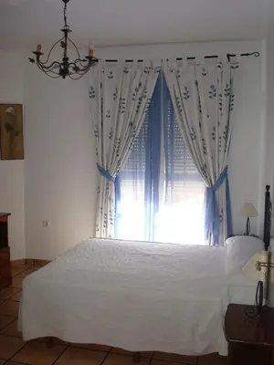 a bedroom with a bed with blue curtains and a window at Hotel Restaurante El Duque in Medina Sidonia