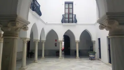 a white building with arches and a black door at Dúplex centro, climatizado, garaje, piscina, WIFI in Sanlúcar de Barrameda