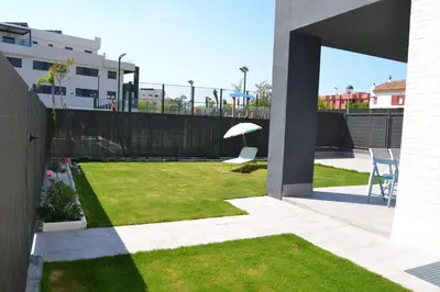 a backyard with a lawn with chairs and an umbrella at Residencial Costa Doñana (Sanlucar de Barrameda) in Sanlúcar de Barrameda