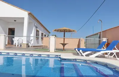 a swimming pool with two chairs and an umbrella at Casa El Cortijillo in Conil de la Frontera