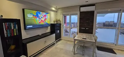 a living room with a television and a table with a laptop at Espectacular ático en 1°linea playa in Rota