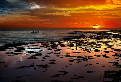a sunset over the ocean with a boat in the water at Mi pequeño apartamento in Cádiz