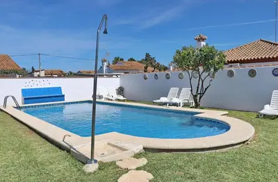a swimming pool in a yard with two lawn chairs at Bungalow Ramos in Conil de la Frontera
