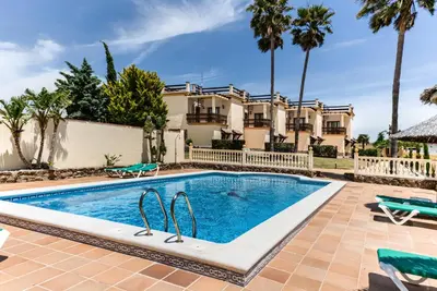a pool in front of a house with palm trees at Apartamentos Villafaro Conil in Conil de la Frontera