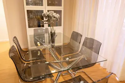 a glass table with four chairs and a vase of flowers at Alquileres Kakiko in Sanlúcar de Barrameda