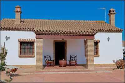 a small white house with two chairs on a patio at Chalet Puente de Tabla in Conil de la Frontera
