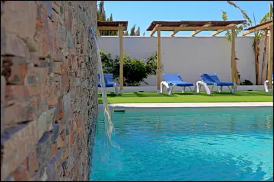 a swimming pool with blue chairs next to a wall at Bungalow La Roa IV in Conil de la Frontera