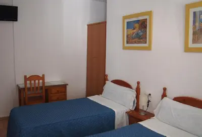 a bedroom with two beds and a desk and a chair at Hostal Fantoni in Cádiz