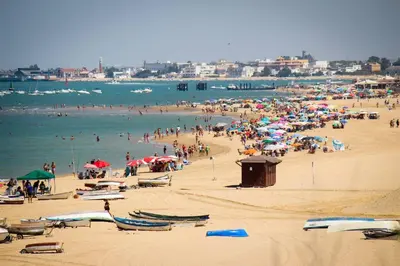 a crowd of people on a beach with umbrellas at Playa de la Calzada in Sanlúcar de Barrameda