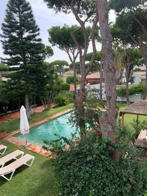 a pool with two lawn chairs and a tree at Villa Cai in Chiclana de la Frontera