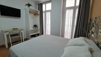 a bedroom with a bed and a tv and windows at Hostal Canalejas in Cádiz