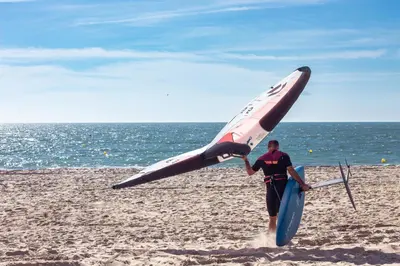 a man on the beach holding a surfboard and a boat at TAIGA Puerto Santa María in El Puerto de Santa María