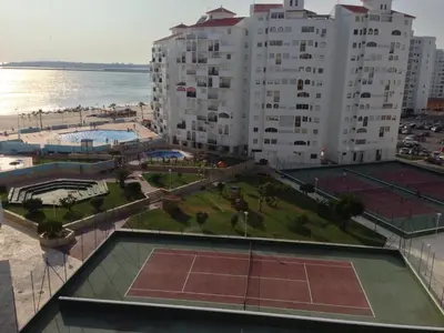a tennis court in front of a large building at Piso frente la playa de Valdelagrana in El Puerto de Santa María