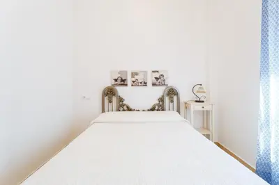 a bed in a white room with two pictures on the wall at Bonito apartamento en campo de golf con piscina in Sanlúcar de Barrameda