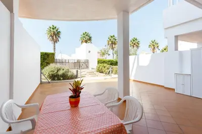 a dining room with a table and white chairs at Bonito apartamento en campo de golf con piscina in Sanlúcar de Barrameda