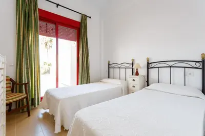 two beds in a bedroom with a window at Bonito apartamento en campo de golf con piscina in Sanlúcar de Barrameda