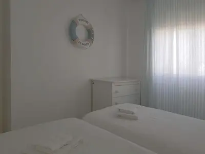 a white bedroom with two beds and a clock on the wall at Valdelagrana Mar Ha Apartment in El Puerto de Santa María