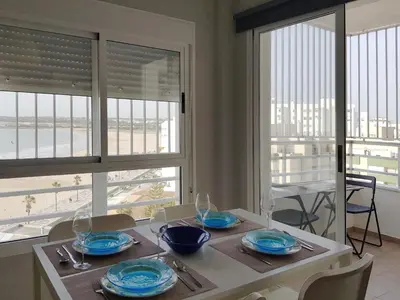 a dining room with a table and chairs and windows at Valdelagrana Mar Ha Apartment in El Puerto de Santa María