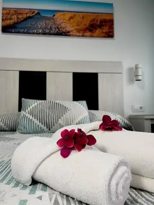 two towels on a bed with red flowers on them at Hostal Los Mellizos in Conil de la Frontera