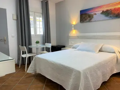 a bedroom with a large white bed and a table at Hostal Los Mellizos in Conil de la Frontera