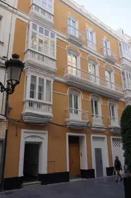 a yellow building with balconies and a woman walking past it at Apartamento Calle Nueva in Cádiz