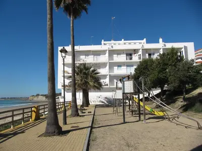 a building on a beach with palm trees and a playground at Life Apartments Fuentebravía in El Puerto de Santa María
