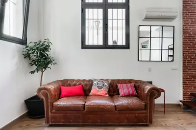 a brown leather couch with three pillows on it at SH El Teatro. Dúplex industrial en el Falla. in Cádiz