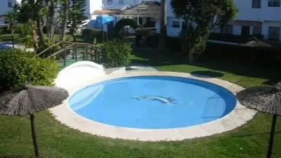 a large blue swimming pool with umbrellas in a yard at Precioso duplex con piscina en Real de la Barrosa in Chiclana de la Frontera