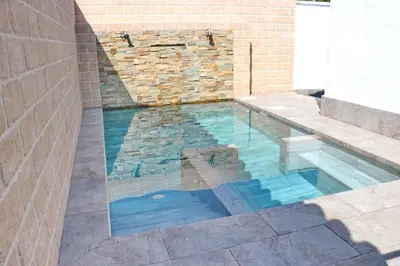 a swimming pool with a bench and a brick wall at Bungalow La Roa II in Conil de la Frontera