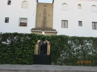 a building with a clock tower behind a hedge at CALLE YERBABUENA 5 in Sanlúcar de Barrameda