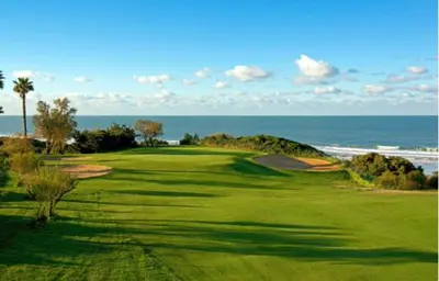 a green golf course with the ocean in the background at Pinar 12 in Chiclana de la Frontera