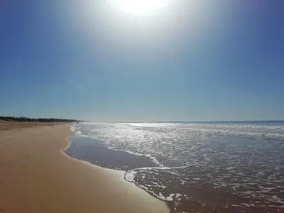 a beach with the sun shining on the water at Pinar 12 in Chiclana de la Frontera
