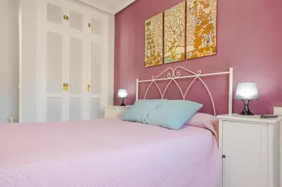a bedroom with a bed with a pink wall at Pinar 12 in Chiclana de la Frontera