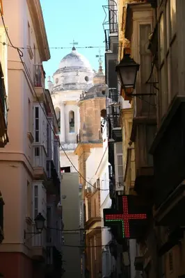 a view of a cathedral from between buildings with a red cross at Apartamento Plaza la Fuente in Cádiz